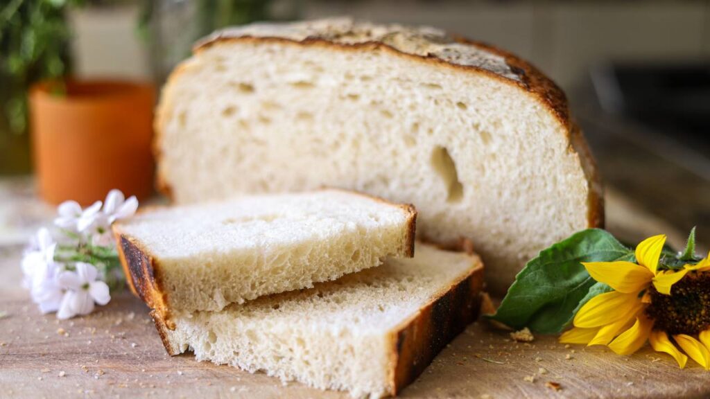 Two slices of sourdough bread on a wooden board with a sunflower and small white flowers.