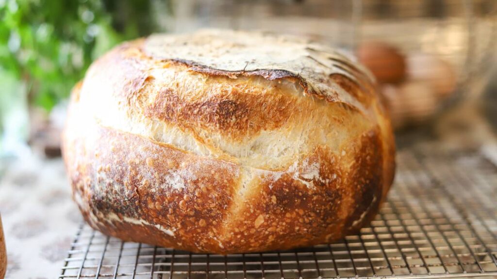 Golden crusted round loaf of sourdough bread cooling on a wire rack.