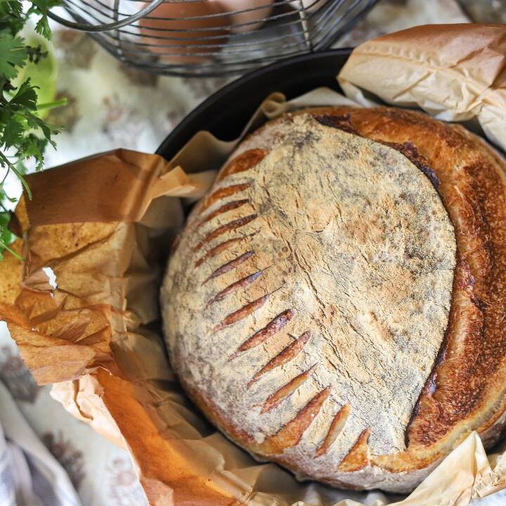 Top-down view of a baked sourdough loaf with scored crust in a Dutch oven.