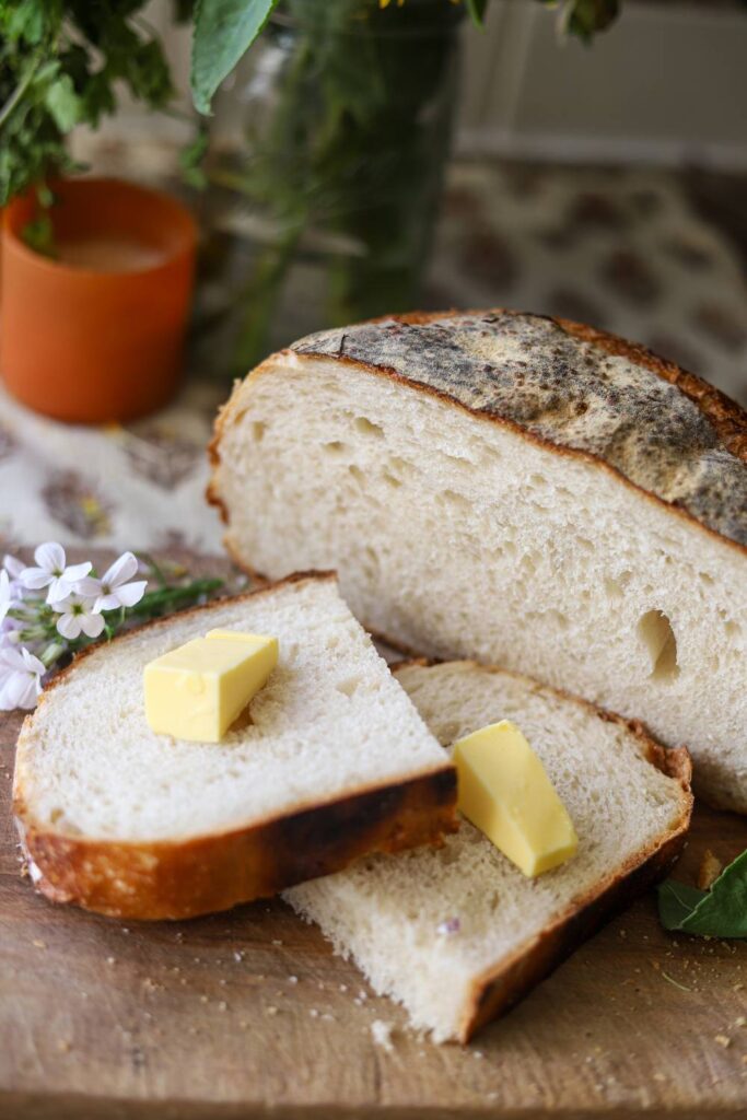 Sliced sourdough bread with pats of butter on top, sitting on a wooden board.