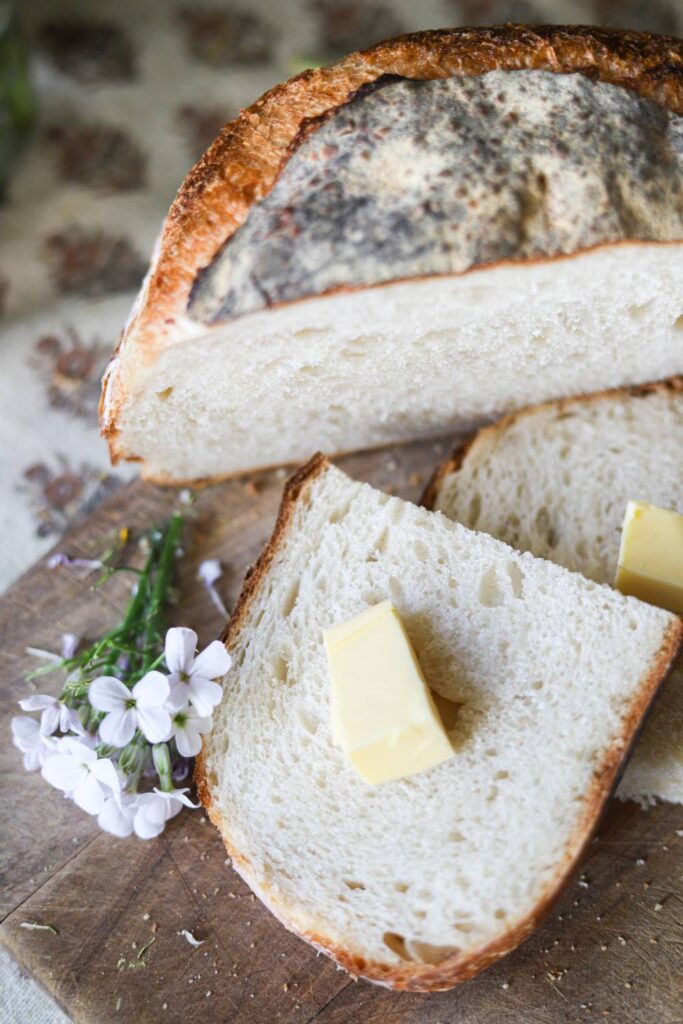 Close-up of sliced sourdough bread with butter and small white flowers.
