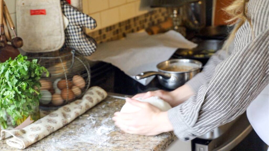 Woman kneading bread dough on a floured countertop in a homey kitchen.