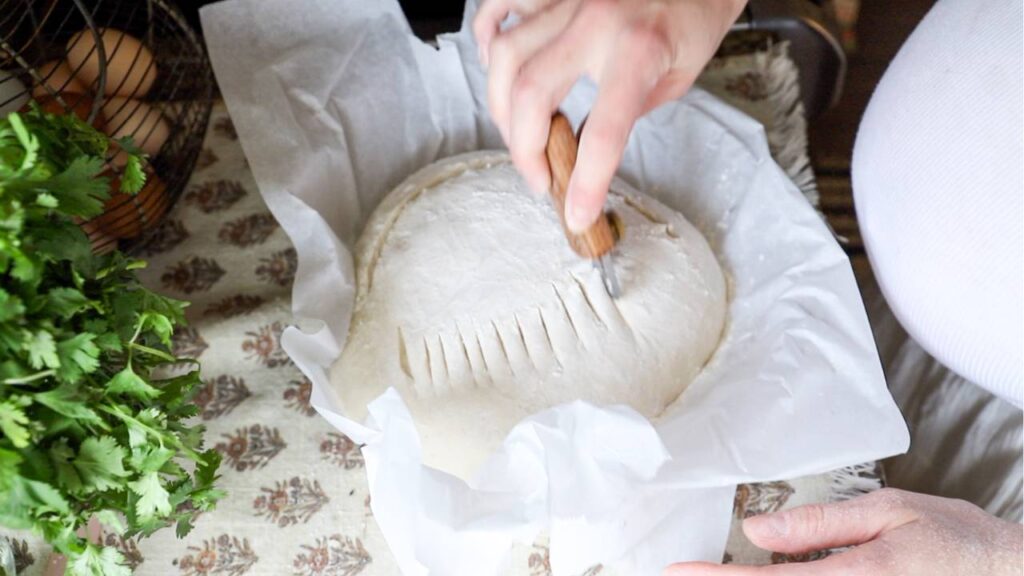 Scoring a round loaf of sourdough dough with a bread lame before baking.