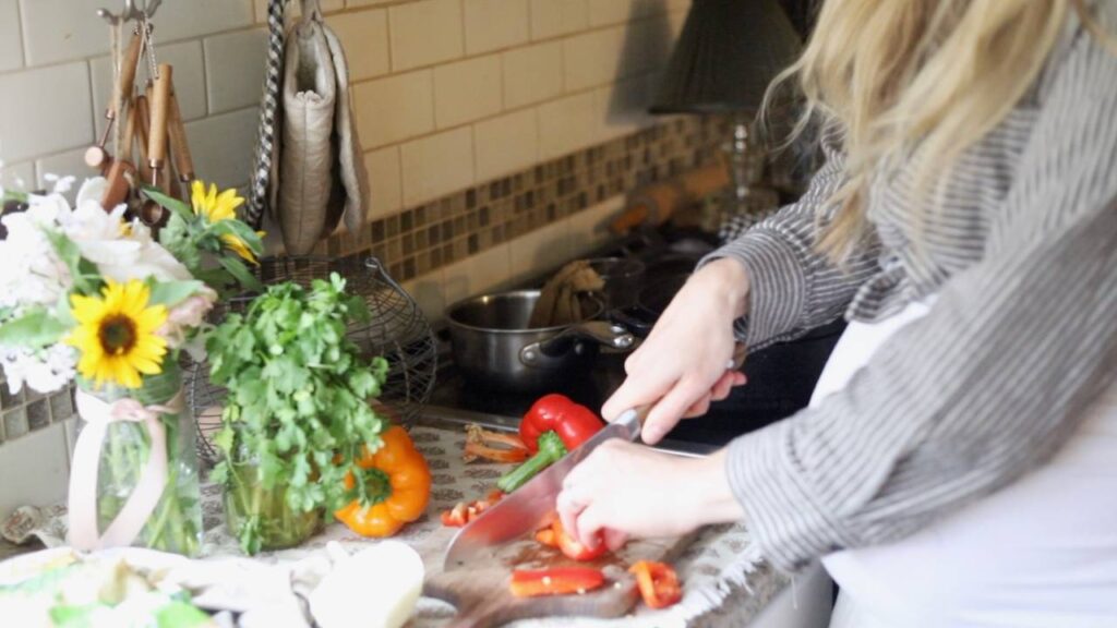 Woman slicing red bell pepper on a kitchen counter.