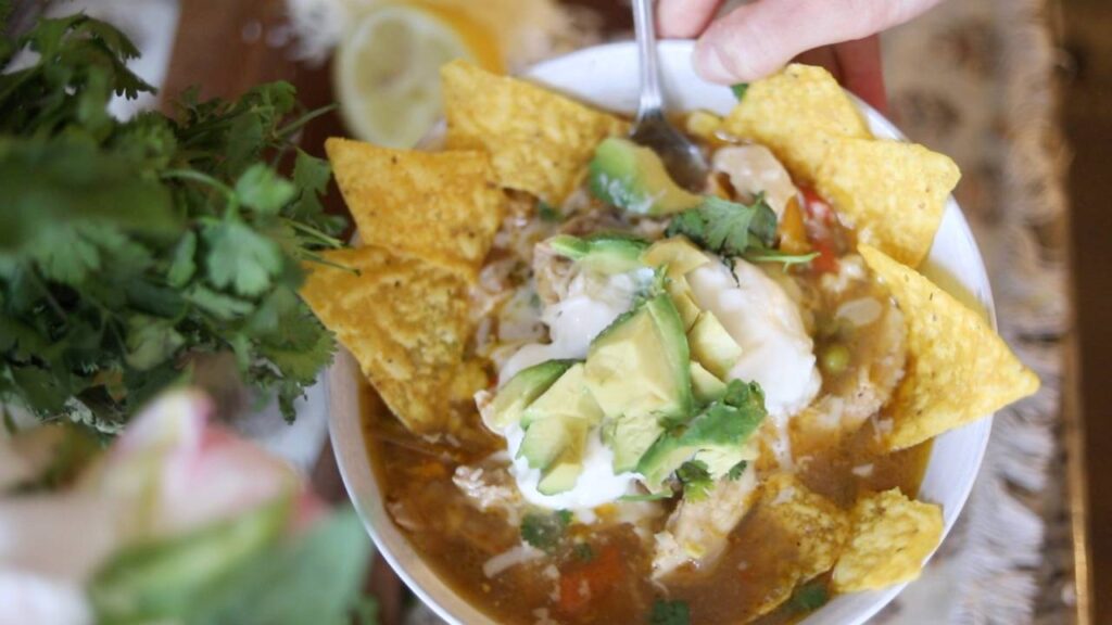 Bowl of chicken tortilla soup topped with avocado, sour cream, and tortilla chips.