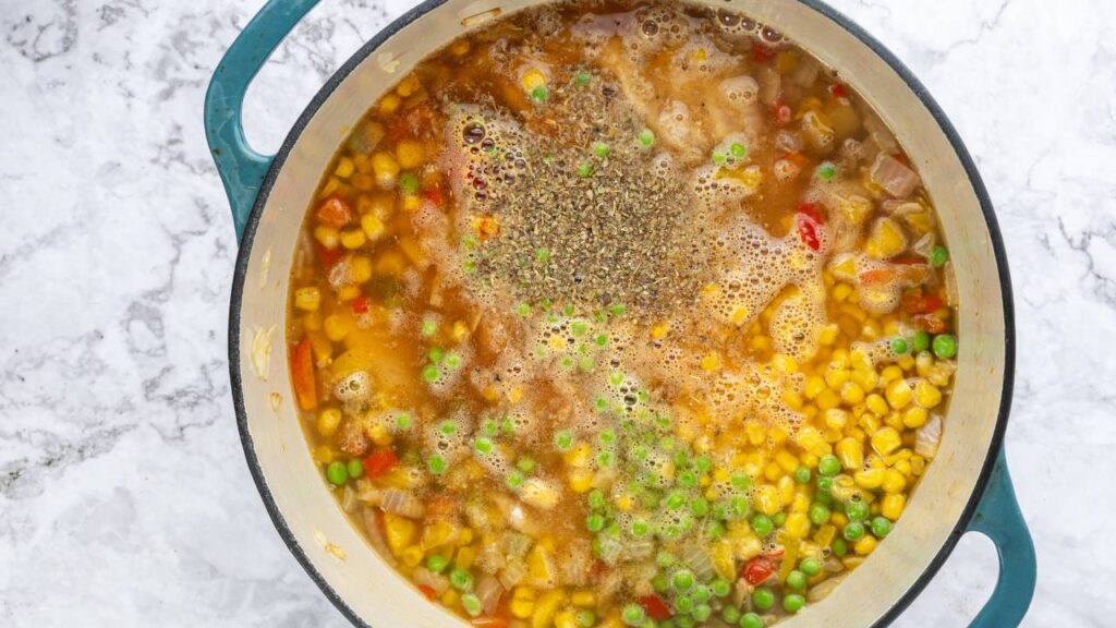 Pot of simmering chicken tortilla soup with corn, peas, peppers, and seasonings.