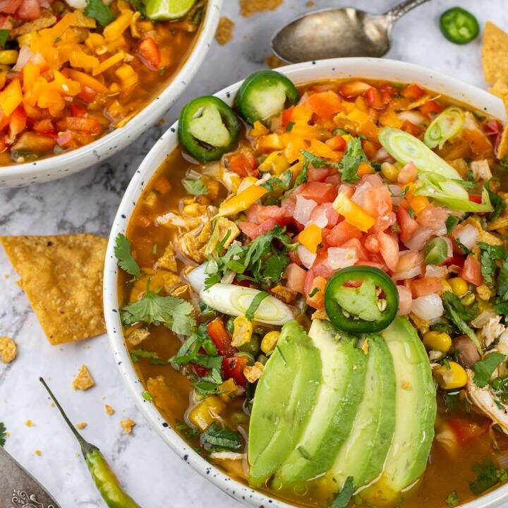 Close-up of chicken tortilla soup with avocado slices, diced vegetables, cilantro, jalapeños, and lime.