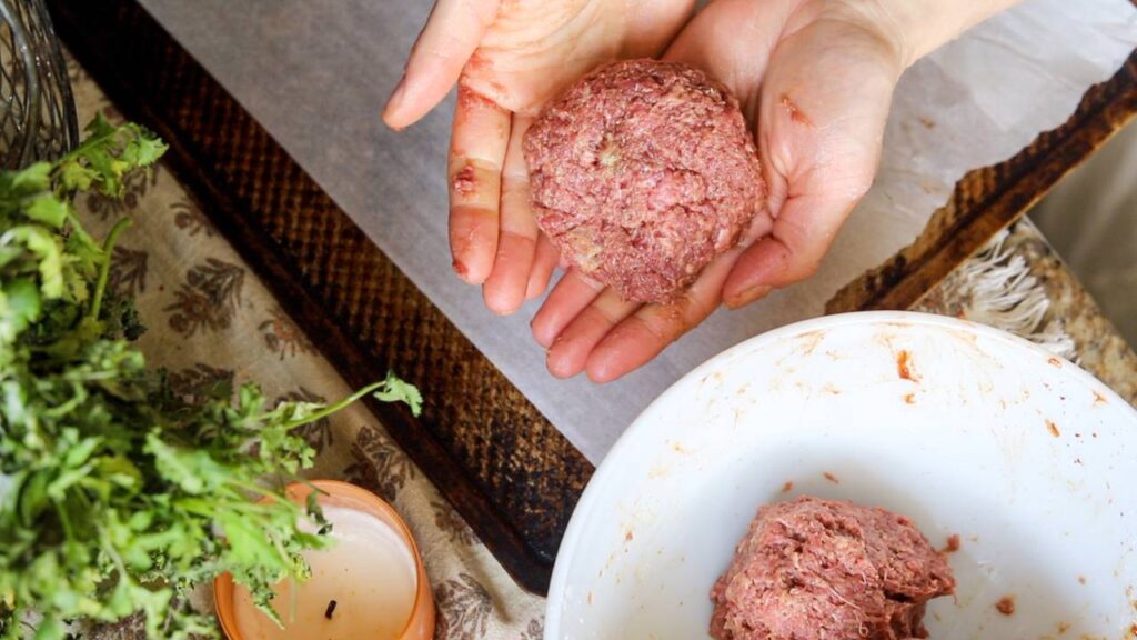 Hands holding a raw hamburger patty over a bowl of ground meat.