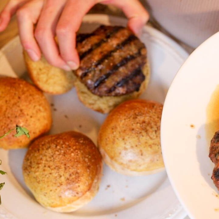 Grilled burger patties being placed on sandwich buns for assembling burgers.