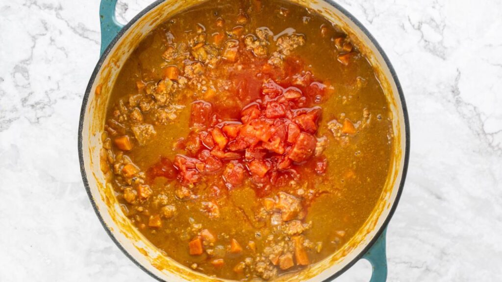 Pumpkin chili simmering in a large pot with diced tomatoes added on top.