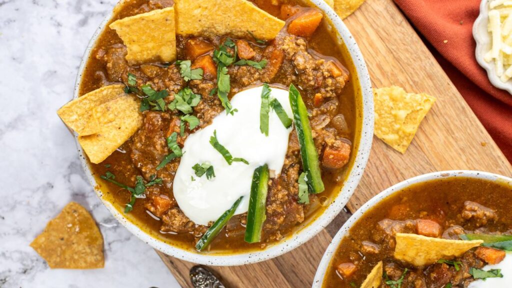 Close-up overhead shot of pumpkin chili in a bowl with sour cream, shredded cheese, herbs, and tortilla chips.