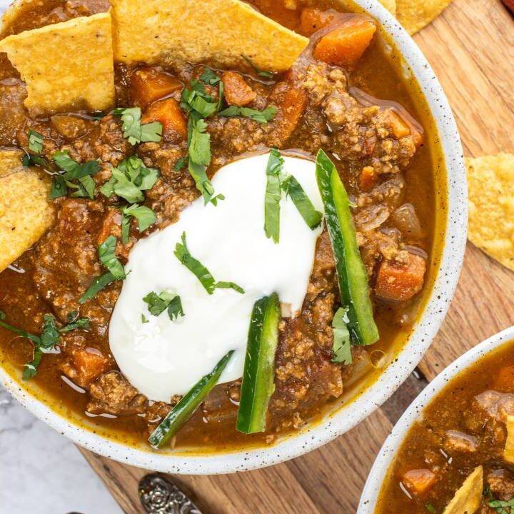 Close-up overhead shot of pumpkin chili in a bowl with sour cream, shredded cheese, herbs, and tortilla chips.