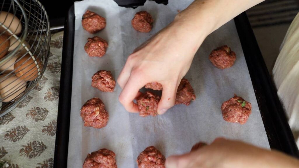 Placing raw meatballs on a baking sheet lined with parchment paper.