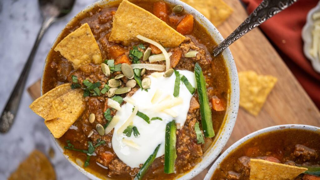 Overhead view of two bowls of pumpkin chili with sour cream, pumpkin seeds, and tortilla chips.