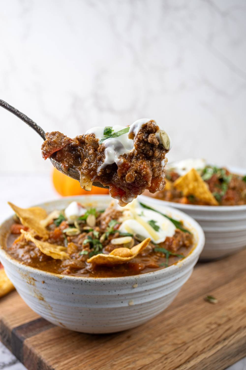 Spoon lifting a hearty scoop of pumpkin chili with sour cream from a bowl.