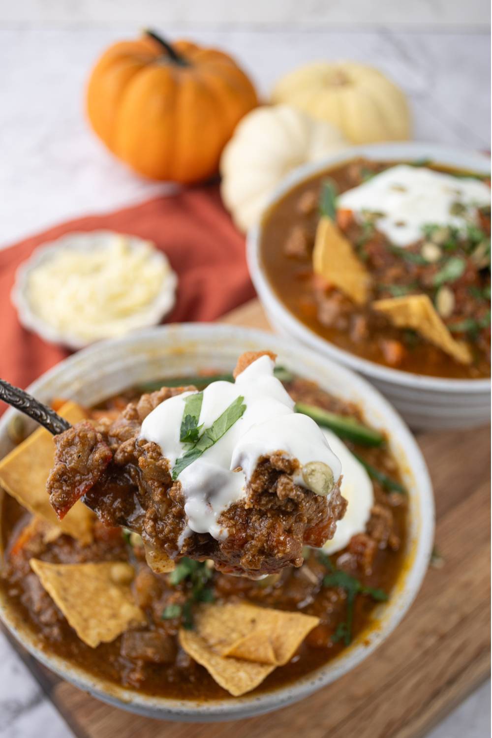 Close-up of a spoonful of pumpkin chili topped with sour cream and herbs over a bowl of chili.