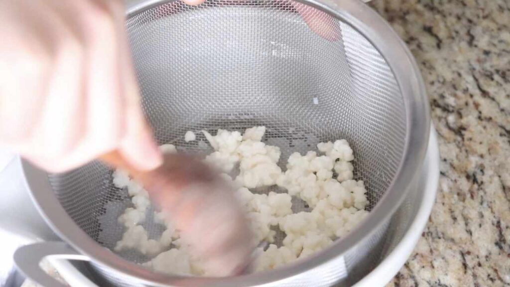 straining kefir grains with a wooden spoon