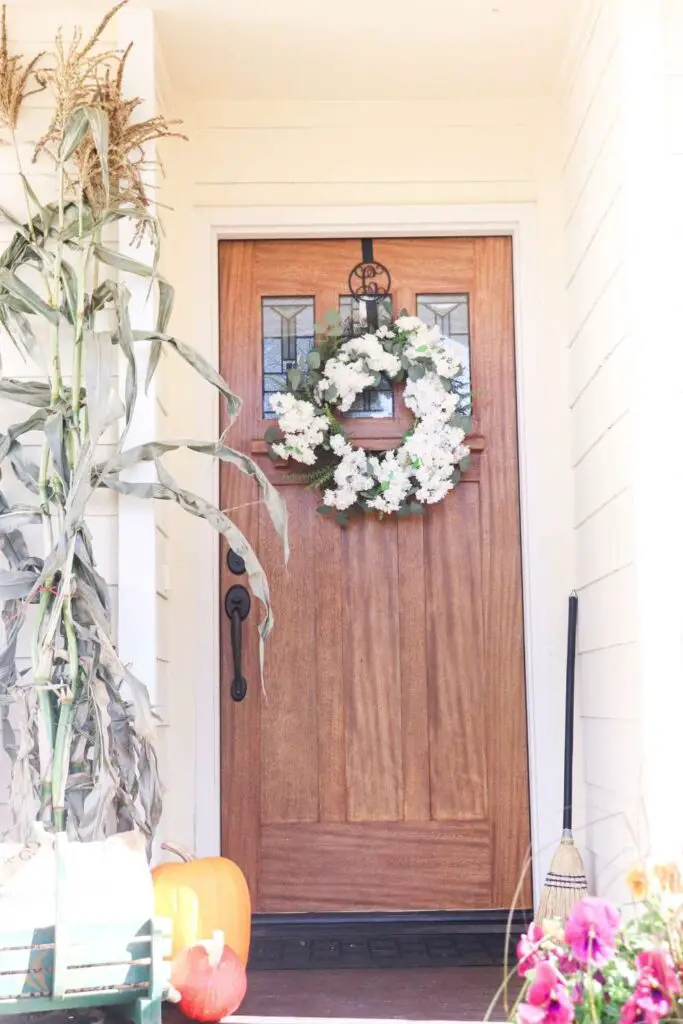 front porch with white wreath, cornstalk, and pumpkins