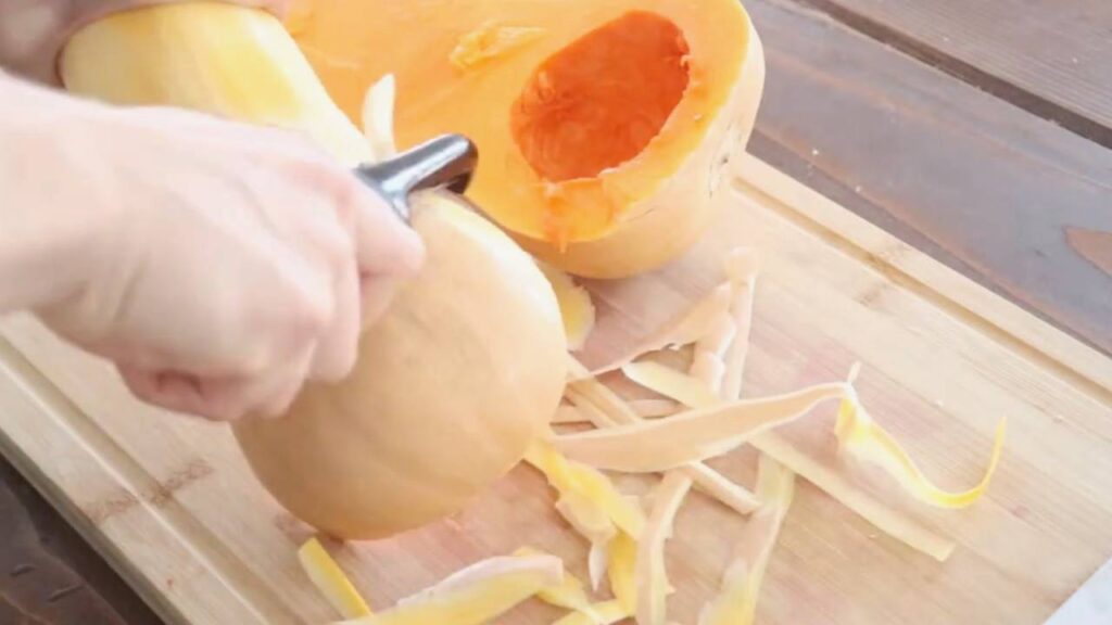 peeling a butternut squash on a wooden cutting board