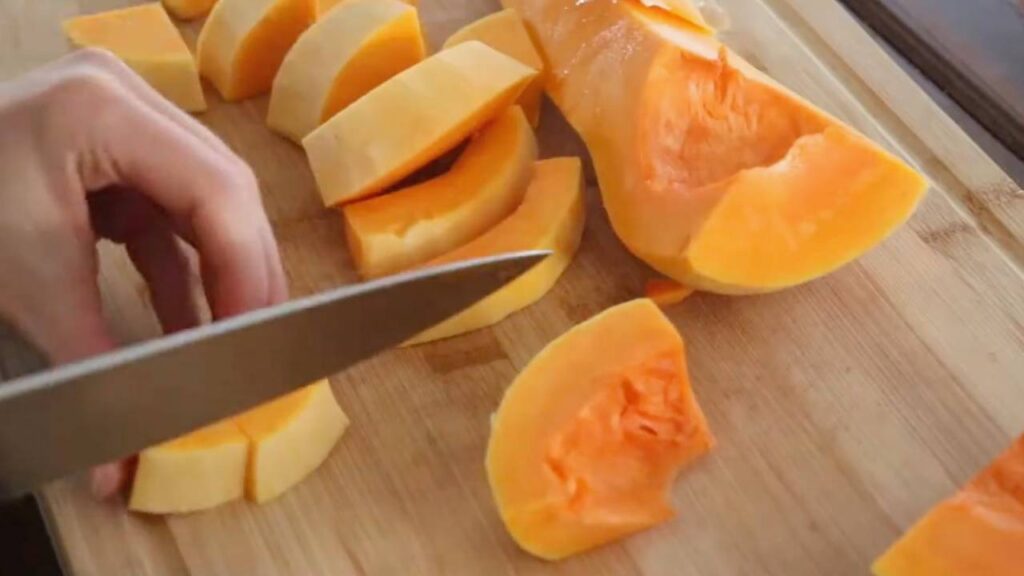 dicing up butternut squash into smaller pieces on a wooden cutting board