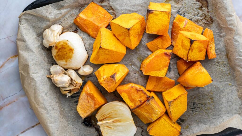Roasted butternut squash, garlic, and onion pieces on a baking sheet lined with parchment paper.