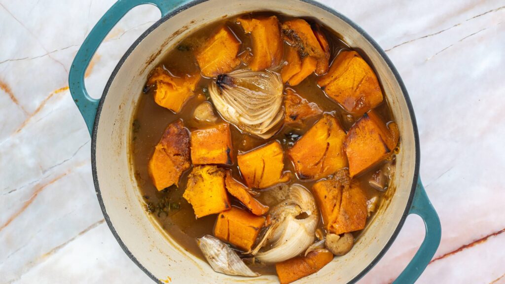 Dutch oven filled with roasted butternut squash, onions, and garlic in broth.