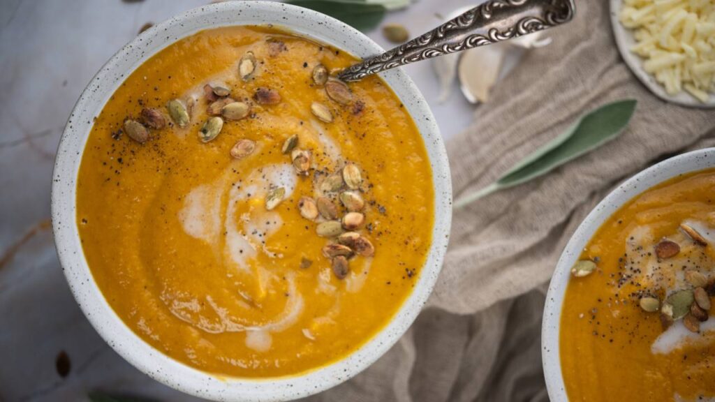 Bowl of butternut squash soup with roasted pumpkin seeds and black pepper sprinkled on top.