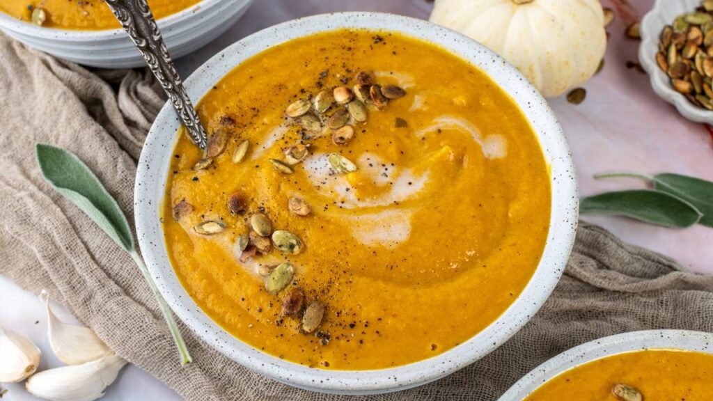 Top view of three bowls of butternut squash soup garnished with cream and roasted seeds.