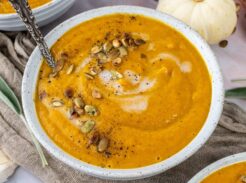 Top view of three bowls of butternut squash soup garnished with cream and roasted seeds.