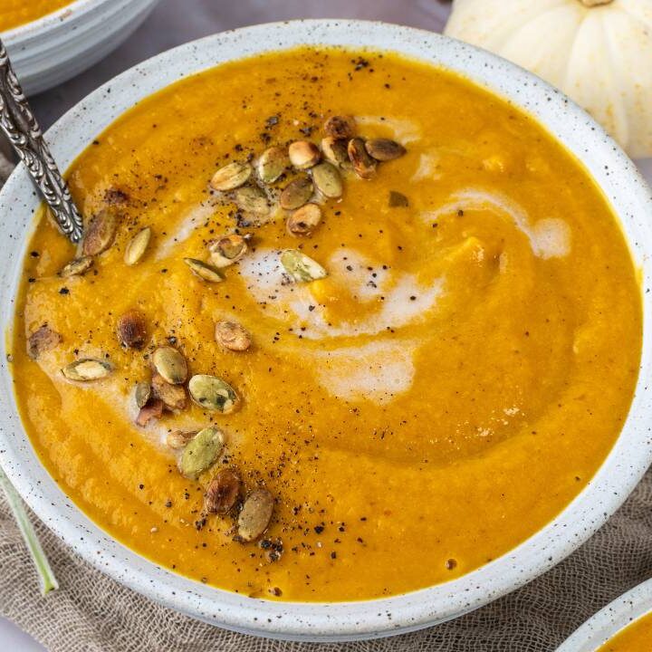 Top view of three bowls of butternut squash soup garnished with cream and roasted seeds.