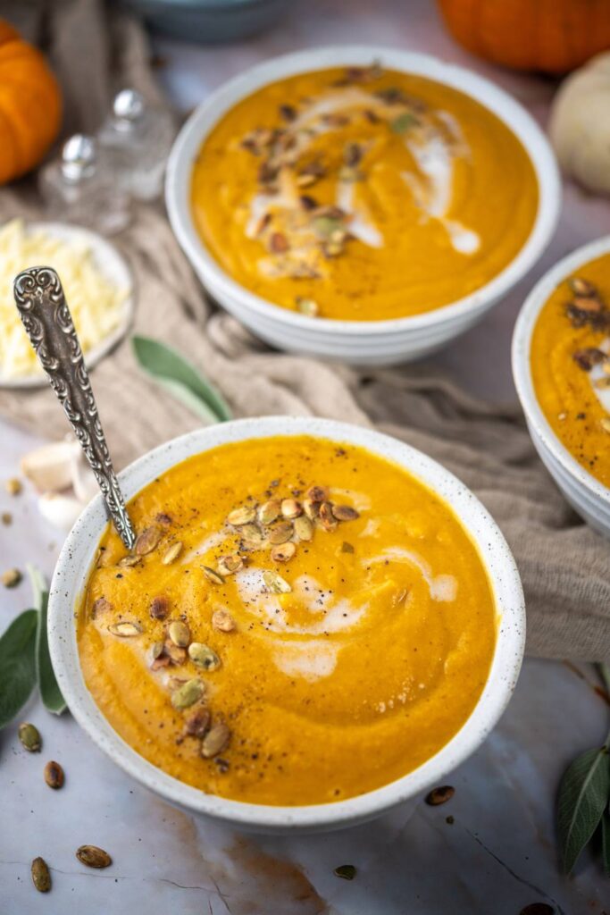 Bowl of butternut squash soup with a spoon, topped with roasted pumpkin seeds and cream.
