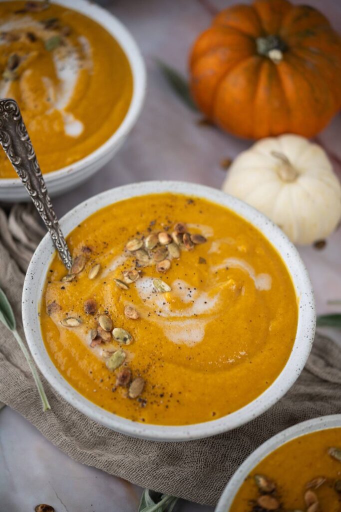 Close-up of three bowls of butternut squash soup with roasted seeds and a spoon in one bowl.