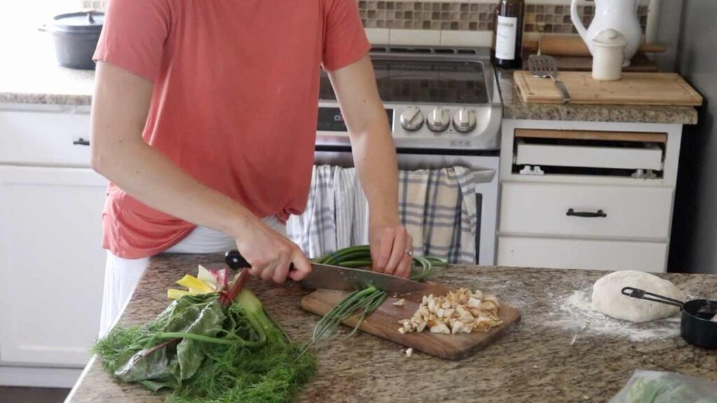 woman cutting up vegetables fennel, garlic scapes, and chicken to make pizza for lunch