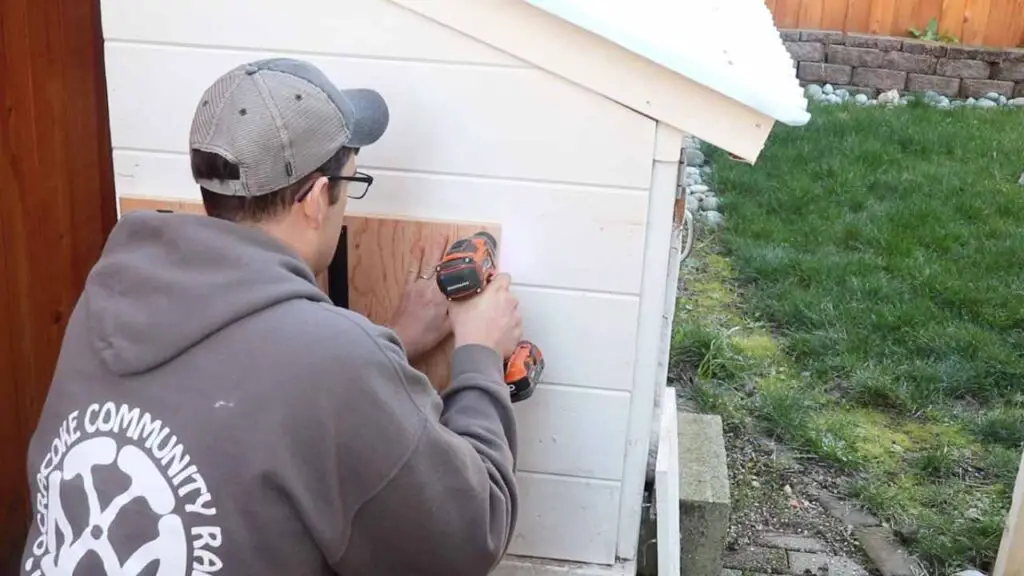 man drilling an automatic chicken coop door to a chicken coop