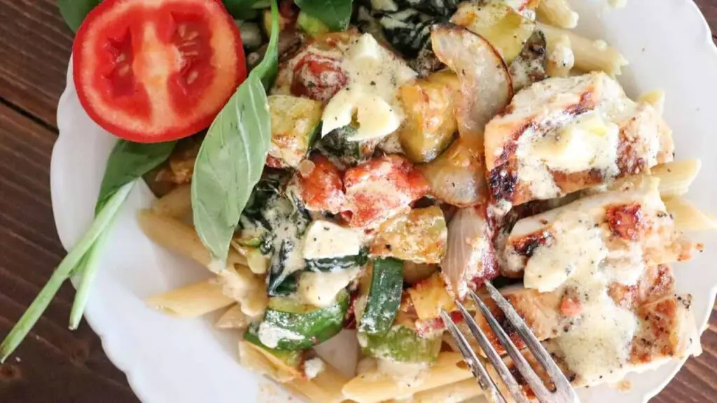 creamy basil chicken pasta on a white dish with a garnish of roma tomato and fresh basil