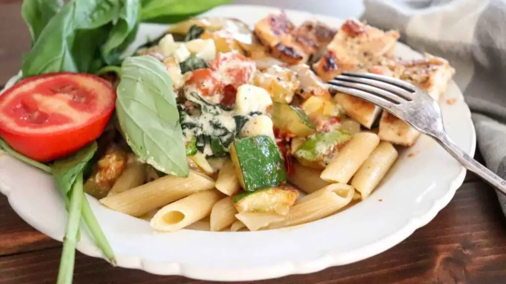 creamy basil chicken pasta on a white dish with a garnish of fresh basil and roma tomato
