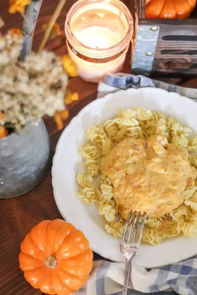 White bowl with pasta and creamy pumpkin carrot pasta sauce, on a farmhouse table with a candle and orange mini pumpkin