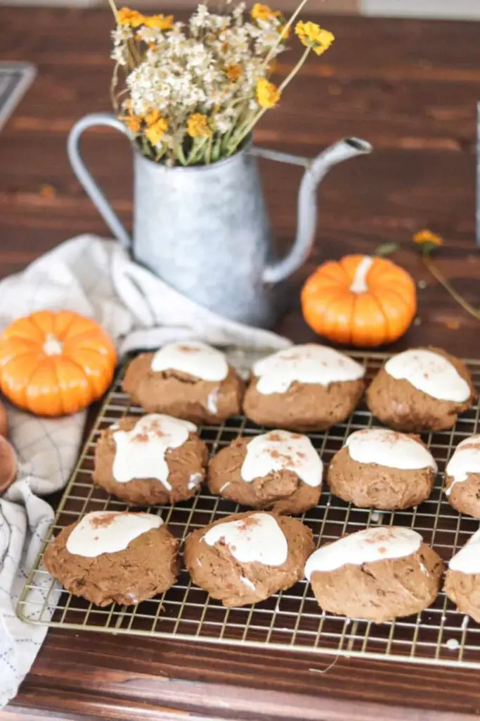 iced pumpkin cookies with sourdough discard cooling on a rack with a galvanized watering can holding a fall bouquet