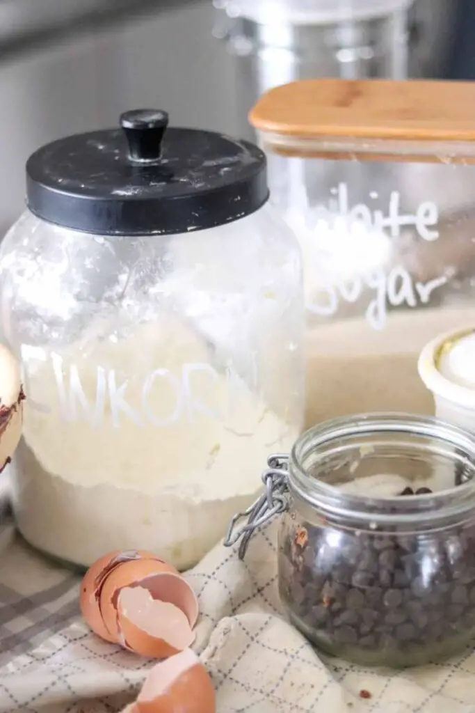 jars of einkorn flour, sugar, and chocolate chips, and brown eggshells on a blue and white cloth