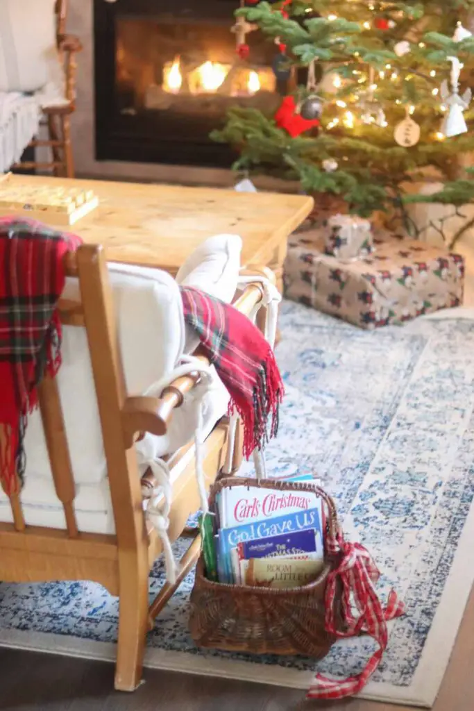 basket of Christmas books next to a chair with a plaid throw blanket, with Christmas tree in the background
