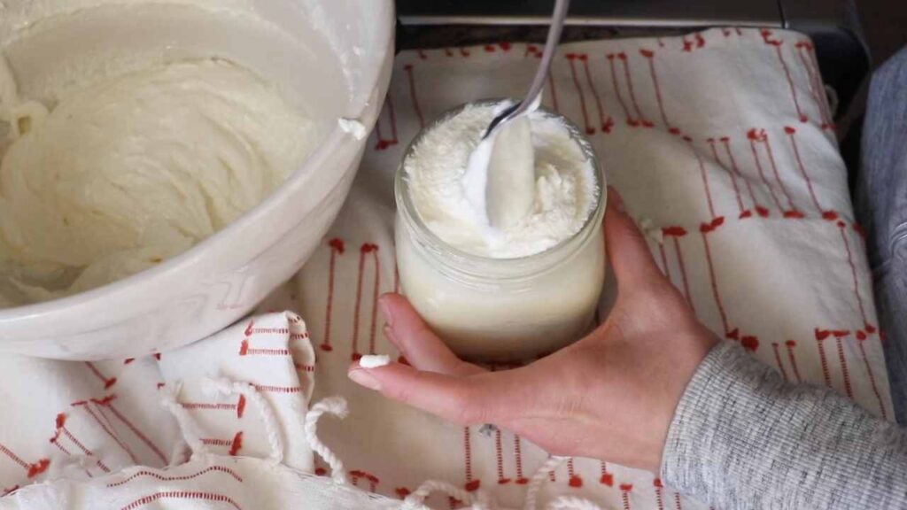 spooning homemade body butter into a mason jar