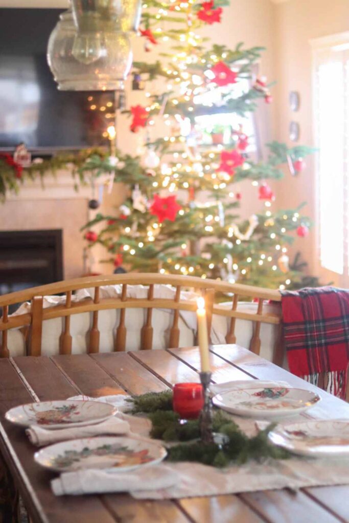 Farmhouse dining table with a simple Christmas tablescape, with Christmas tree in the background