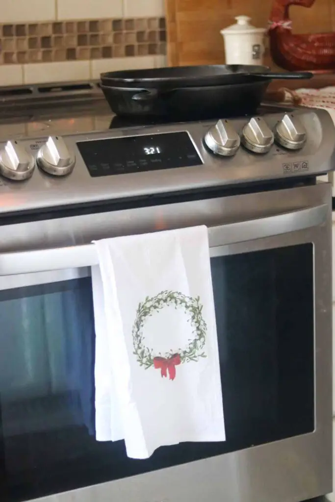 white tea towel with Christmas wreath, hanging on oven