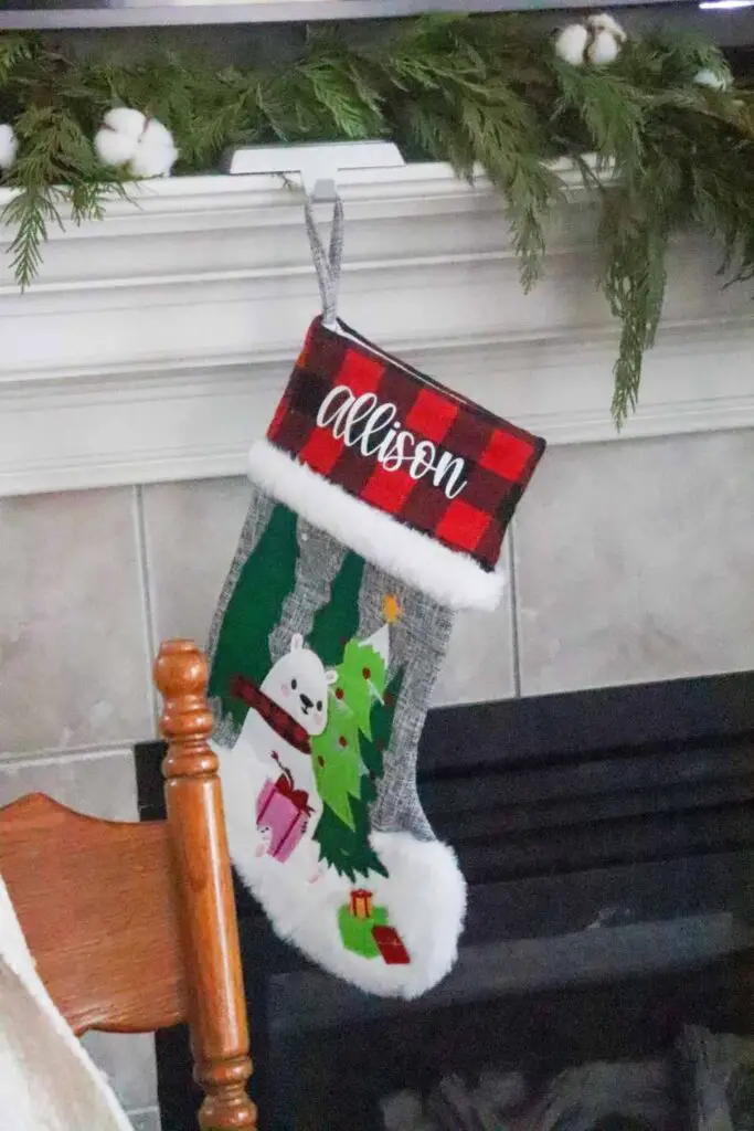 a child's Christmas stocking hanging on a fireplace mantel decorated with pine garland and cotton