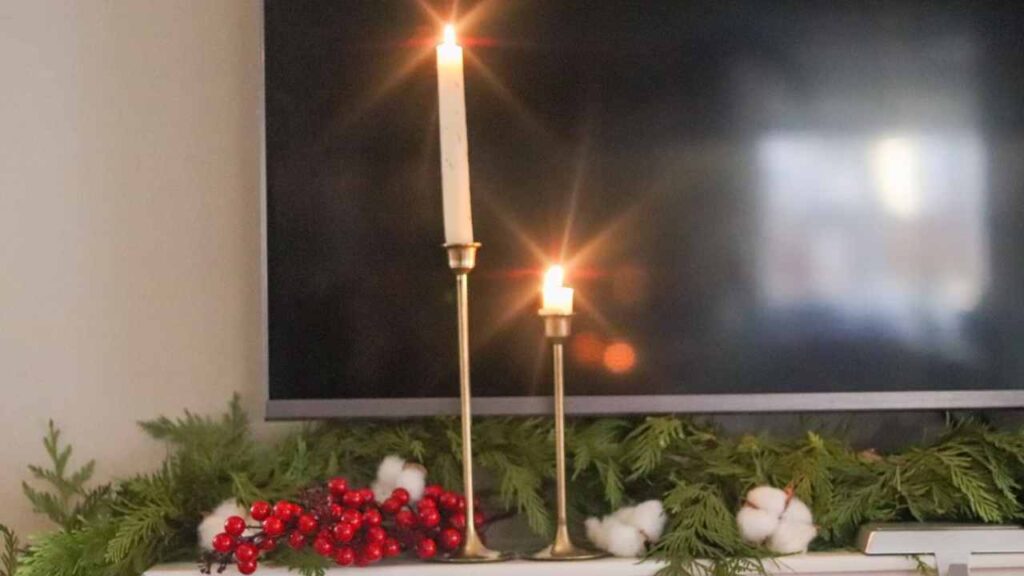 fireplace mantel decorated for Christmas with fresh pine garland, cotton, cranberries, and brass candlesticks