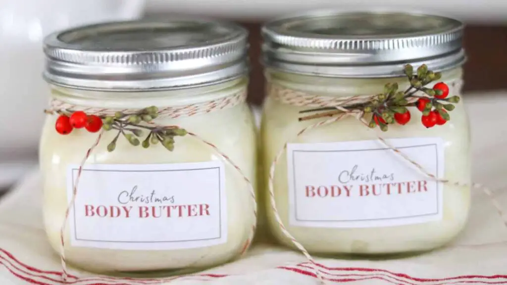 Two jars of homemade Christmas body butter, decorated with bakers twine and juniper sprigs