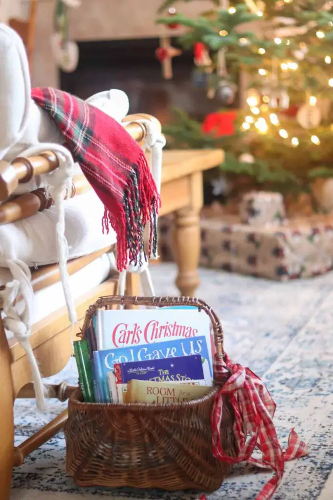 basket of Christmas books next to a chair with a plaid throw blanket, with Christmas tree in the background