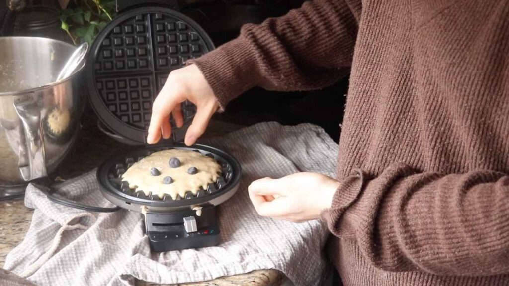 Adding fresh blueberries to homemade einkorn waffle batter in a waffle maker