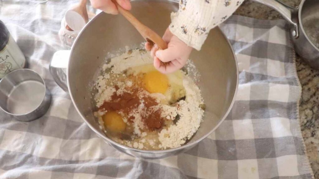 Toddler's hand adding ingredients for homemade einkorn waffles to bowl of a stand mixer