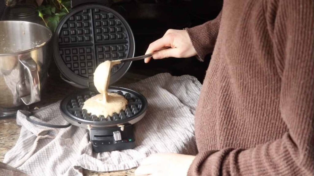 Using a ladle to spoon homemade einkorn waffle batter into a waffle maker